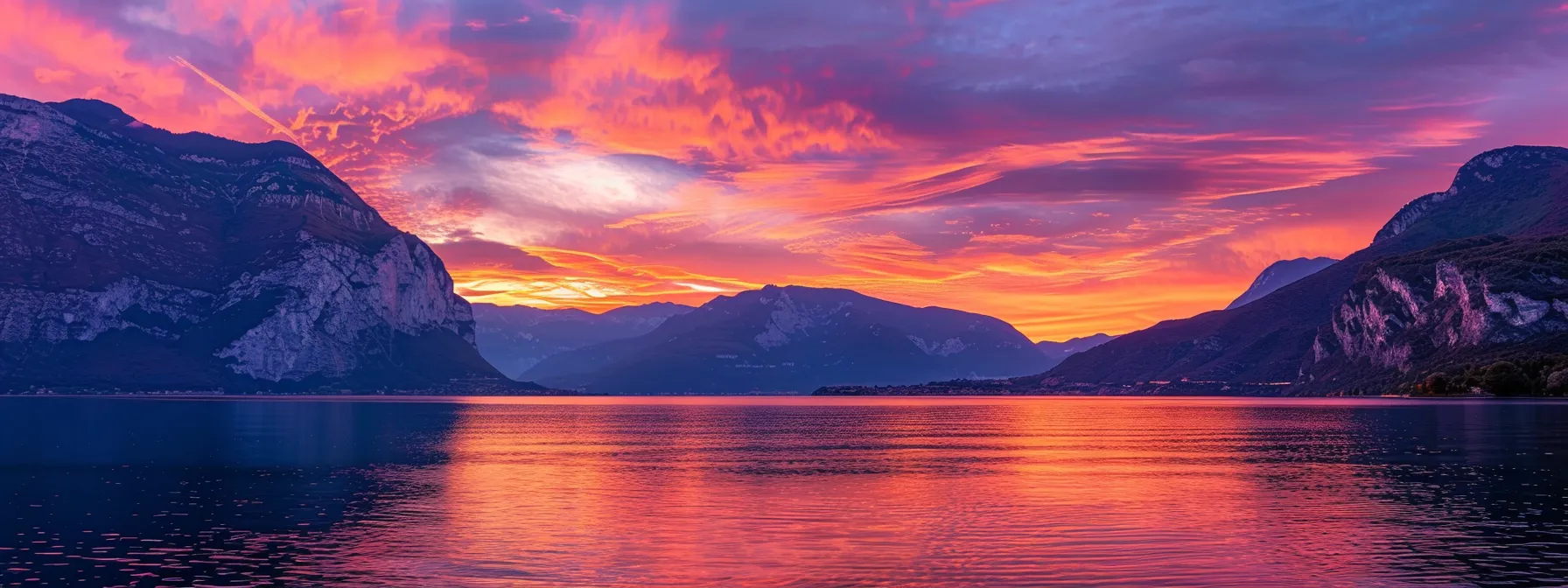 a breathtaking sunset illuminates a serene lake, casting vibrant reflections of fiery orange and soft purple hues across the calm water surface.